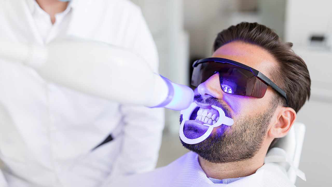 Closeup of a dental patient sitting down, wearing sun glasses, while a teeth whitening is being performed