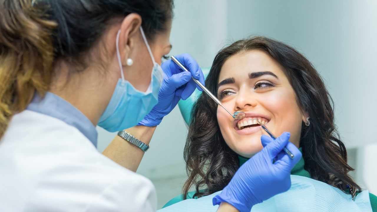 Closeup of female patient sitting in a dentist chair smiling while a dentist checks her teeth