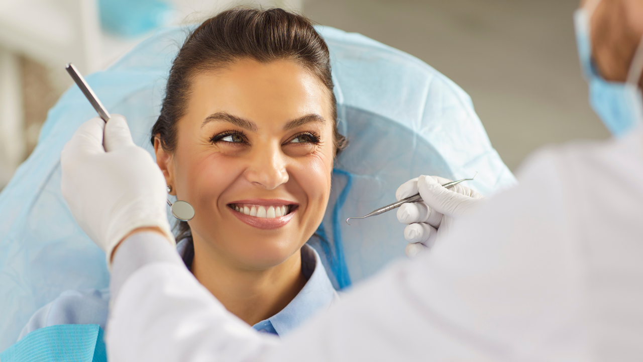 Closeup of a woman sitting in the dentist chair, smiling, while the dentist holds tools close to her mouth